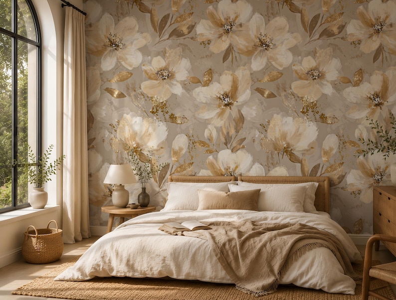 May include: A bedroom featuring wallpaper with a large-scale floral pattern in shades of cream, beige, and metallic gold. The bed has a light-coloured duvet, a textured throw blanket, and several pillows. A wooden nightstand holds a lamp and vase.