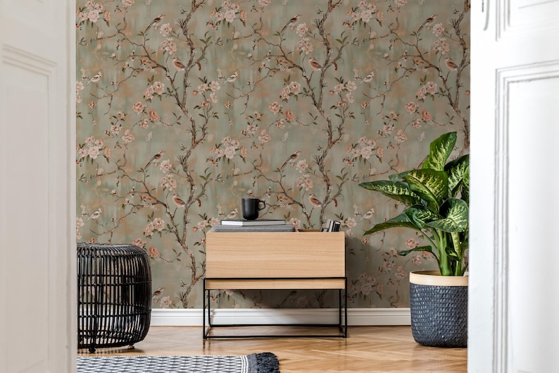 May include: Wallpaper featuring a repeating pattern of brown tree branches with light pink flowers and small birds against a muted sage green background. The design includes delicate floral details and avian figures spread across the surface.