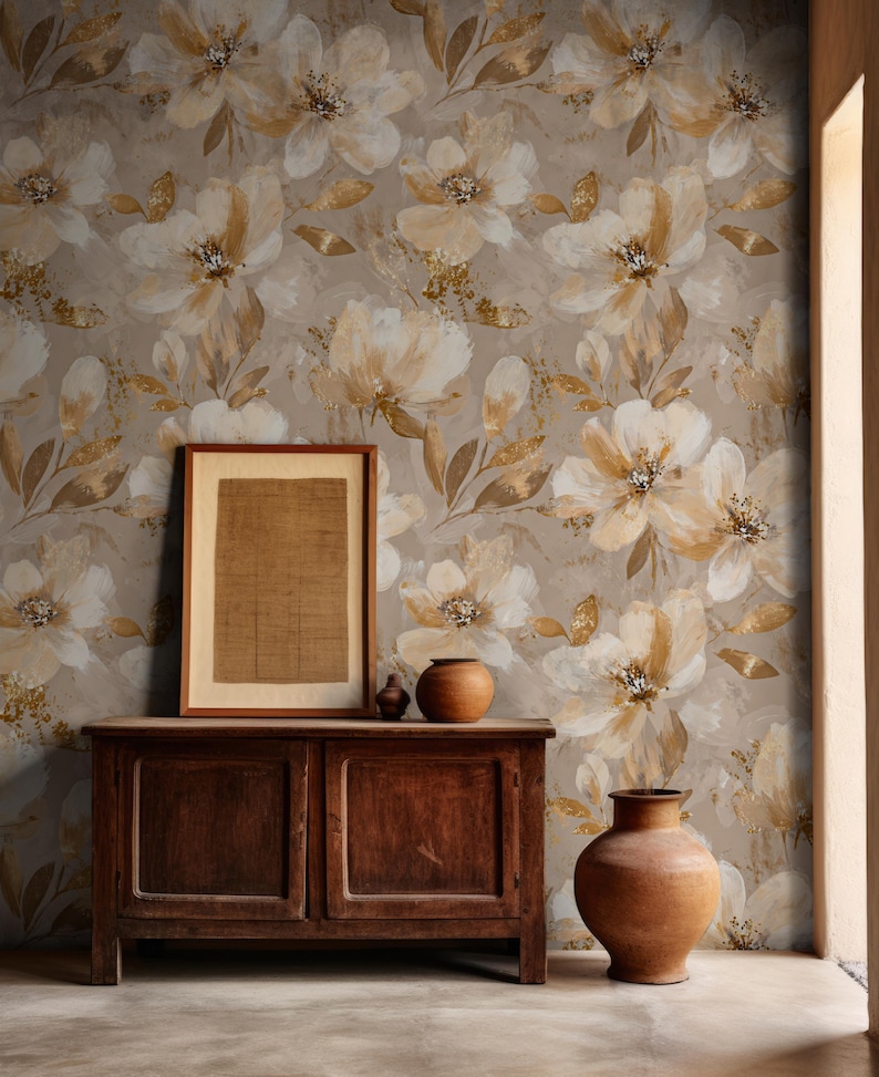 May include: A dark wooden cabinet with two doors stands against a wall covered in wallpaper featuring a large-scale floral pattern in shades of beige, cream, and gold. A framed rectangular print and two rounded clay vases sit on the cabinet top.