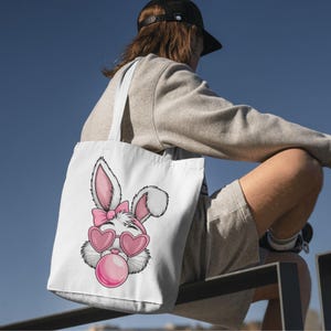 May include: White tote bag with a pink bunny wearing pink heart-shaped sunglasses and blowing a pink bubble. The bunny has a pink bow on its head.