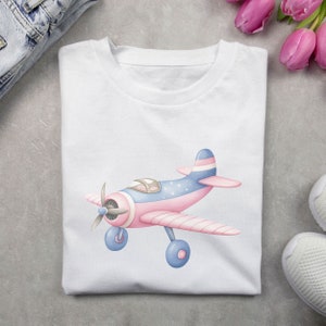 May include: A white t-shirt with a pink and blue airplane graphic. The airplane has white stripes and blue and white polka dots.
