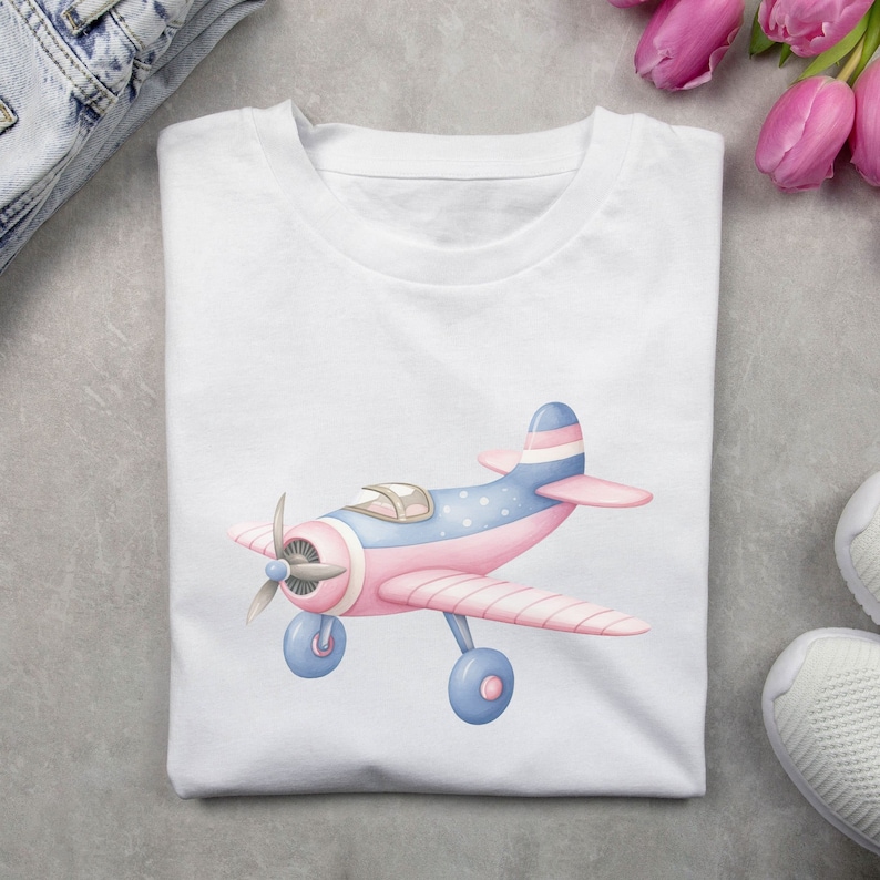May include: A white t-shirt with a pink and blue airplane graphic. The airplane has white stripes and blue and white polka dots.