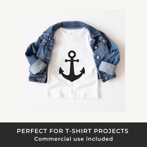 May include: A white t-shirt with a large black anchor graphic, paired with a blue denim jacket. The t-shirt design is simple and nautical. The jacket is folded over the t-shirt.