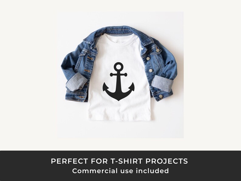 May include: A white t-shirt with a large black anchor graphic, paired with a blue denim jacket. The t-shirt design is simple and nautical. The jacket is folded over the t-shirt.
