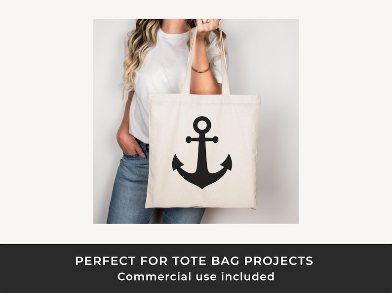 May include: Cream-colored tote bag with a large black anchor design. The bag is held by a person wearing a white t-shirt and blue jeans. The tote bag has a simple, nautical theme.