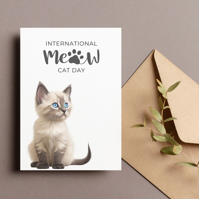 Pu&ograve; includere: Un biglietto di auguri bianco con la scritta "INTERNATIONAL MEOW CAT DAY" e un'illustrazione di un gattino. Il gattino ha gli occhi blu e il pelo marrone chiaro. Una busta e un rametto di verde sono sullo sfondo.