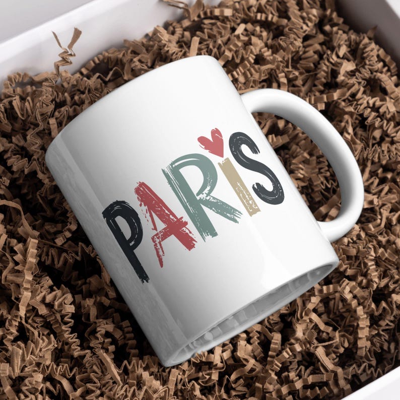 May include: White ceramic mug with a colorful, hand-painted design that says "PARIS" with a red heart above the word.