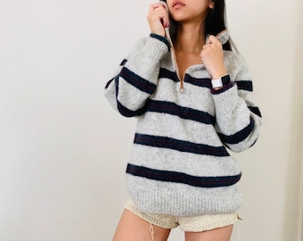 May include: A gray and black striped sweater with a zipper at the neck. The sweater is made of a soft, fuzzy material.
