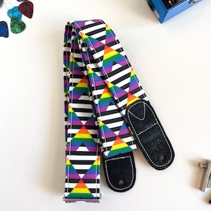 May include: A guitar strap with a black and white striped background and a rainbow triangle pattern. The strap has two black adjustable ends.