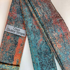 May include: A guitar strap with a blue and orange abstract pattern. The strap is made of fabric and has a label that says "Coco Guitar Straps".