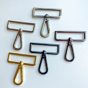 May include: Six different metal swivel clasps with rectangular loops and D-shaped rings. The clasps are in various finishes, including silver, gold, and black.