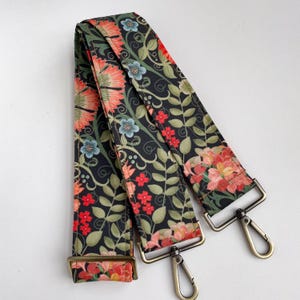 Puede incluir: Una correa ajustable con herrajes de metal dorado, con un patrón floral negro y verde. La correa mide aproximadamente 3,8 cm de ancho.
