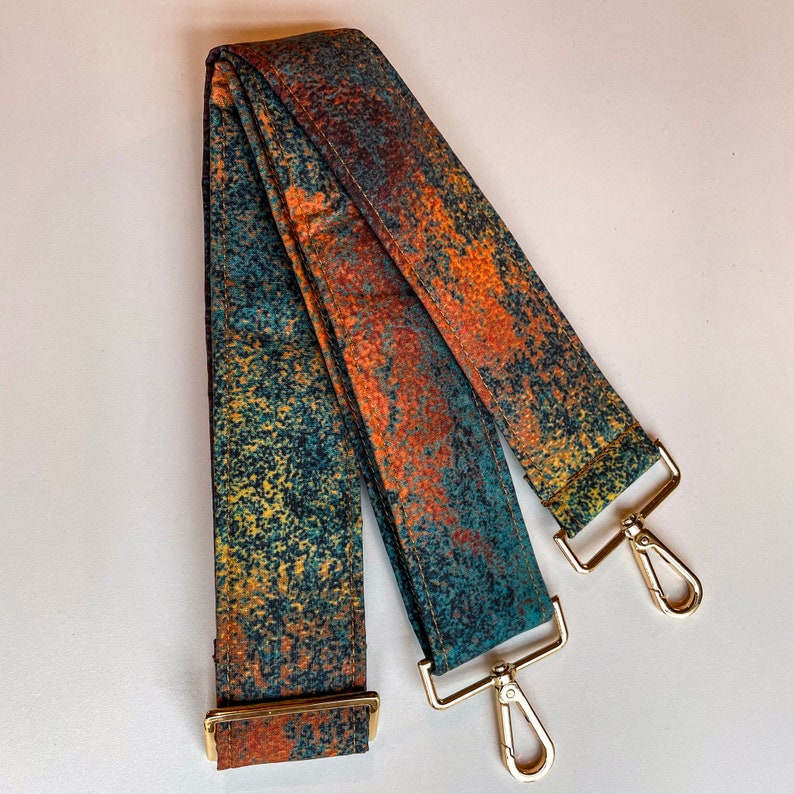 May include: A long, adjustable strap with a blue, green, and orange abstract pattern. The strap has two gold metal clasps.