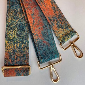 May include: Two adjustable straps with gold metal clasps. The straps are made of a fabric with a blue, green, and orange abstract pattern.
