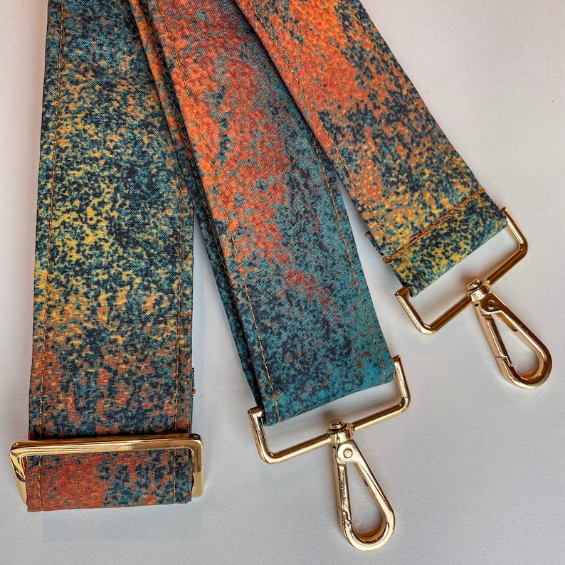 May include: Two adjustable straps with gold metal clasps. The straps are made of a fabric with a blue, green, and orange abstract pattern.