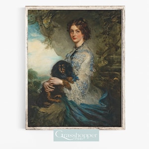 May include: A woman in a white dress with blue embroidery holds a small black dog. The woman is standing in a garden setting with green foliage and a stone wall behind her.