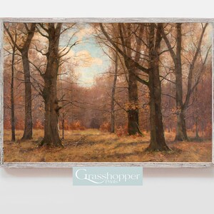 May include: A framed landscape painting depicts a forest scene in autumn. Tall, bare trees with brown trunks and branches dominate the foreground. The ground is covered in dry grass and fallen leaves, with a light blue sky peeking through the trees.