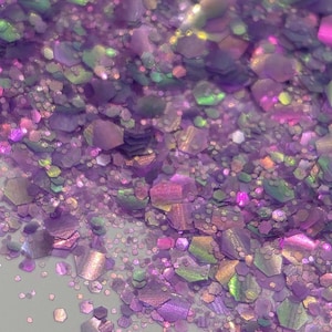 May include: Close-up of iridescent glitter in shades of purple, pink, and green. The glitter pieces are hexagonal and scattered, creating a sparkling effect. Ideal for crafts, nail art, or decorative purposes.