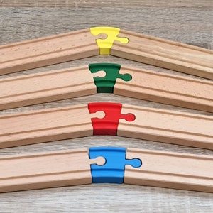 Può includere: Quattro pezzi di binario del treno in legno con diversi pezzi di puzzle colorati che li collegano. I pezzi sono gialli, verdi, rossi e blu.