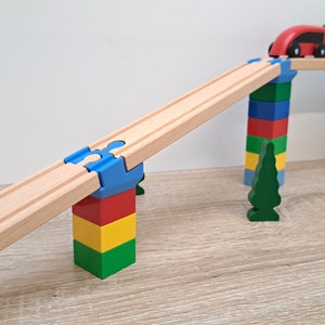 May include: A wooden train track set with a blue, red, yellow, and green wooden block tower, a green wooden tree, and a red and green toy train.