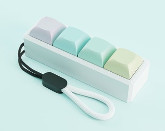 May include: A set of four pastel-colored keycaps in a white plastic case with a black and white lanyard. The keycaps are lavender, light blue, turquoise, and light green.