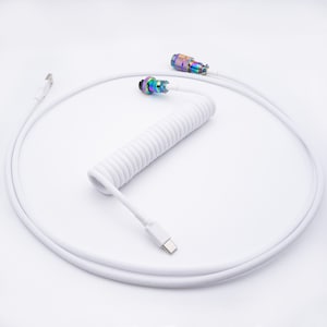 Puede incluir: Cable USB blanco enrollado con un conector USB-C en un extremo y un conector USB-A en el otro extremo. El cable está enrollado y tiene un exterior trenzado blanco.