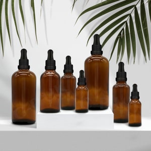 May include: A set of seven amber glass bottles with black dropper tops. The bottles are arranged in a row from largest to smallest, with the largest bottle in the centre.