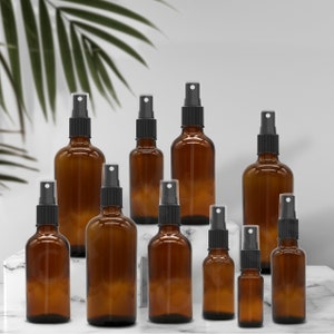 May include: A set of amber glass spray bottles with black spray tops. The bottles are arranged in two rows, with the larger bottles at the front and the smaller bottles at the back. The bottles are on a white marble surface.