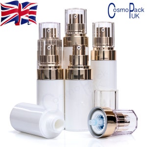 May include: Five white plastic bottles with gold accents and clear pump tops. The bottles are arranged in a group on a white surface. The bottles are empty and ready to be filled with liquid.