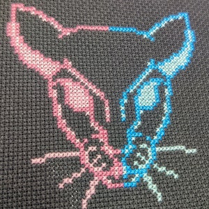 May include: Cross-stitch embroidery of a cat's face, with one half pink and the other half blue.
