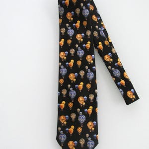 May include: Black necktie featuring a repeating pattern of colorful hot air balloons. The balloons are in shades of blue, orange, and yellow, set against a black background. The tie is made of a smooth fabric.
