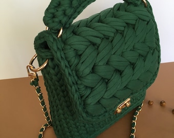 May include: A dark green crocheted handbag with a gold chain strap and a top handle. The bag has a woven texture and a structured shape.