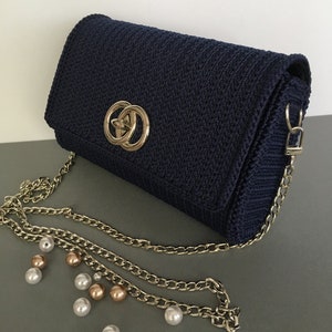 May include: A navy blue woven clutch bag with a gold chain strap and a gold double ring closure.