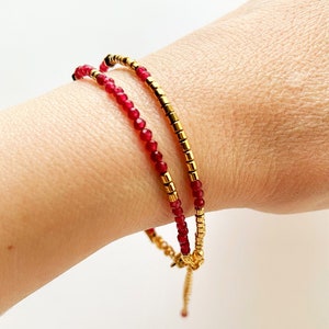 Può includere: Un braccialetto di perline rosse e dorate con chiusura a nodo scorrevole. Il braccialetto è realizzato con piccole perline rotonde e viene indossato al polso.