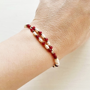 May include: A double-strand bracelet with red and white beads. The bracelet is made with small, round beads and has a gold accent.