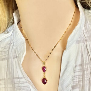 Op de afbeelding: Een gouden ketting met een hanger met twee robijnrode stenen. De grotere steen is rond en de kleinere is druppelvormig.