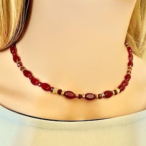 May include: A red gemstone necklace with gold accents. The necklace is made of small, oval-shaped red gemstones and gold beads.
