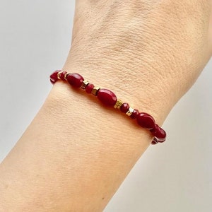 Peut inclure: Un bracelet en pierres précieuses rouges avec des accents dorés. Le bracelet est composé de petites pierres précieuses rouges de forme ovale et de perles dorées.