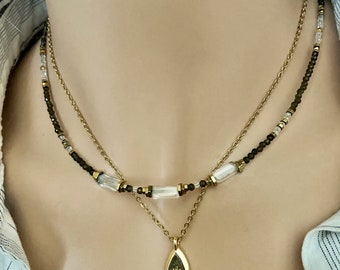 May include: A gold chain necklace with a teardrop pendant featuring a small flower design. The chain is layered with a second chain featuring alternating clear and dark brown beads.