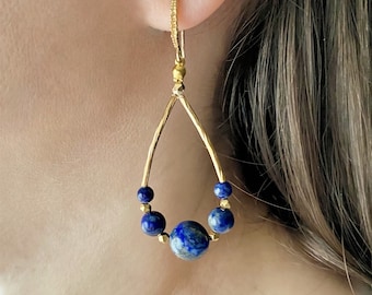 May include: Gold teardrop earrings with a blue lapis lazuli stone and smaller blue beads.