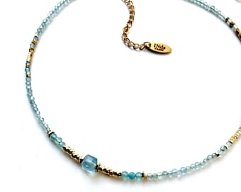 May include: A delicate gold and blue beaded necklace with a square aquamarine gemstone. The necklace features a gold chain closure with a small tag that reads "INDA PARIS".