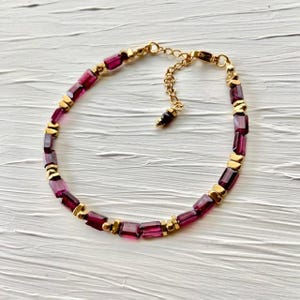 Puede incluir: Un brazalete de oro y piedras preciosas moradas con un delicado extensor de cadena. El brazalete presenta piedras preciosas de forma rectangular.
