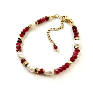 Peut inclure: Un bracelet composé d'une alternance de perles rouges à facettes, de perles blanches irrégulières et de petites entretoises métalliques dorées. Le bijou comprend un fermoir mousqueton doré et une chaînette d'extension avec une perle rouge.