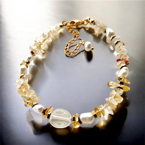 May include: A bracelet with a natural, organic design. It features light-yellow citrine chips, creamy white pearls, and gold-coloured metal accents. The bracelet is secured with a gold-toned clasp and chain. The bracelet's length is adjustable.