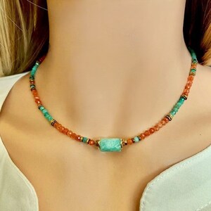 Puede incluir: Un collar delicado con una mezcla de cuentas naranjas y verdes, con una piedra turquesa más grande en el centro.