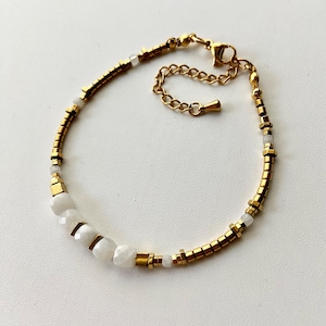 May include: A gold bracelet with white beads and a gold clasp. The bracelet is made of small, square-shaped beads.