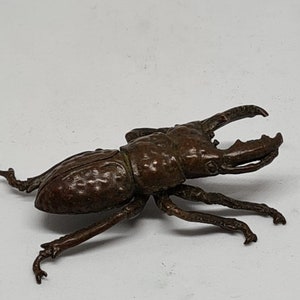 Puede incluir: Una escultura de bronce de un escarabajo ciervo volante con detalles precisos y alas texturizadas.