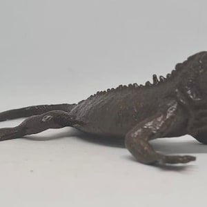 May include: A dark brown plastic toy lizard with a spiky back and a long tail.