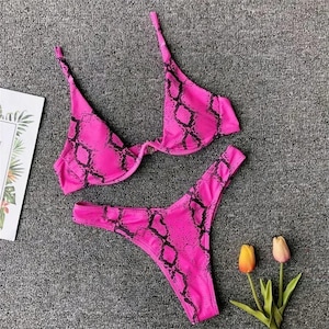 May include: A two-piece bikini set featuring a vibrant hot pink base with a black snakeskin print pattern. The top includes underwire cups and thin shoulder straps, while the bottom is a high-cut style with matching pink and black print.