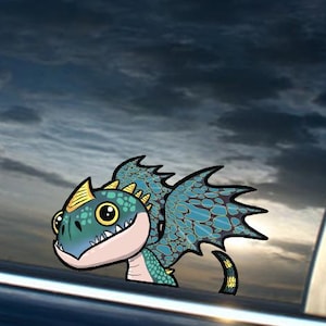 May include: A cartoon dragon sticker is affixed to a car window. The dragon has a teal body, yellow horns, and large yellow eyes. The sticker is against a backdrop of a cloudy sky.